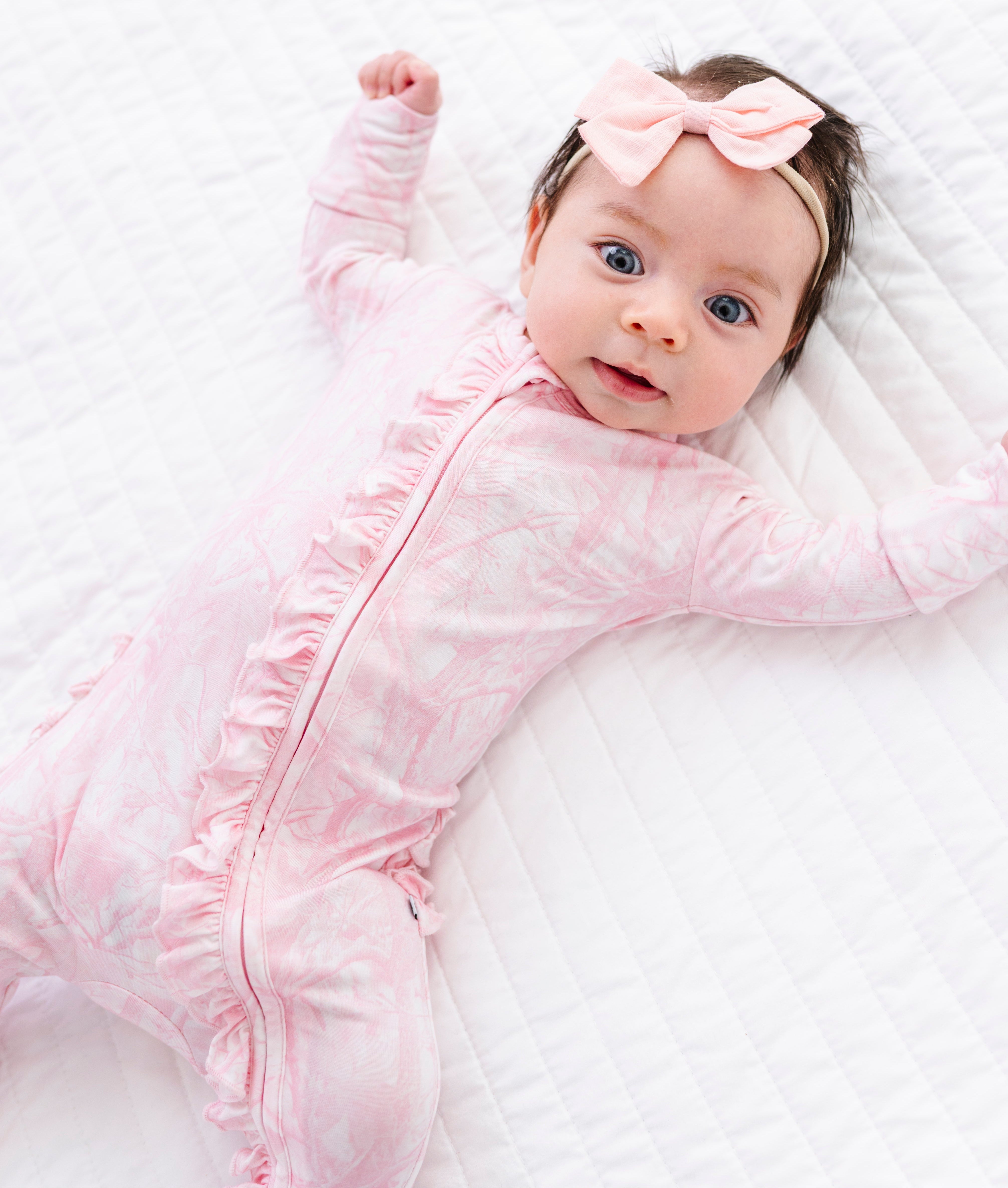 Baby in a pink camo romper with a bow on a white blanket